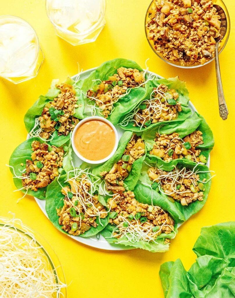 A white plate filled with vegan lettuce wraps topped with rice noodles and centered around a bowl of sriracha mayo