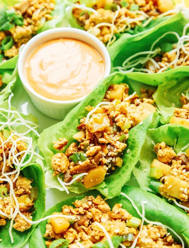 A close-up view of vegan lettuce wraps filled with tofu, veggies, sauce, green onion, and rice noodles