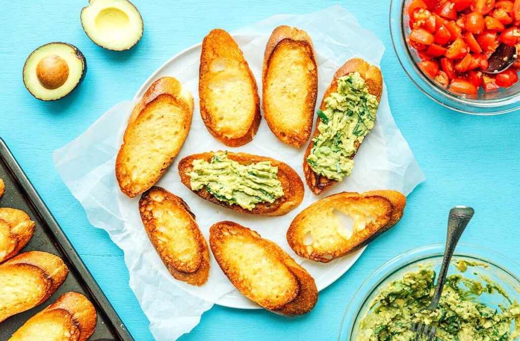 A plate filled with 8 sliced of broiled baguette, 2 covered with avocado