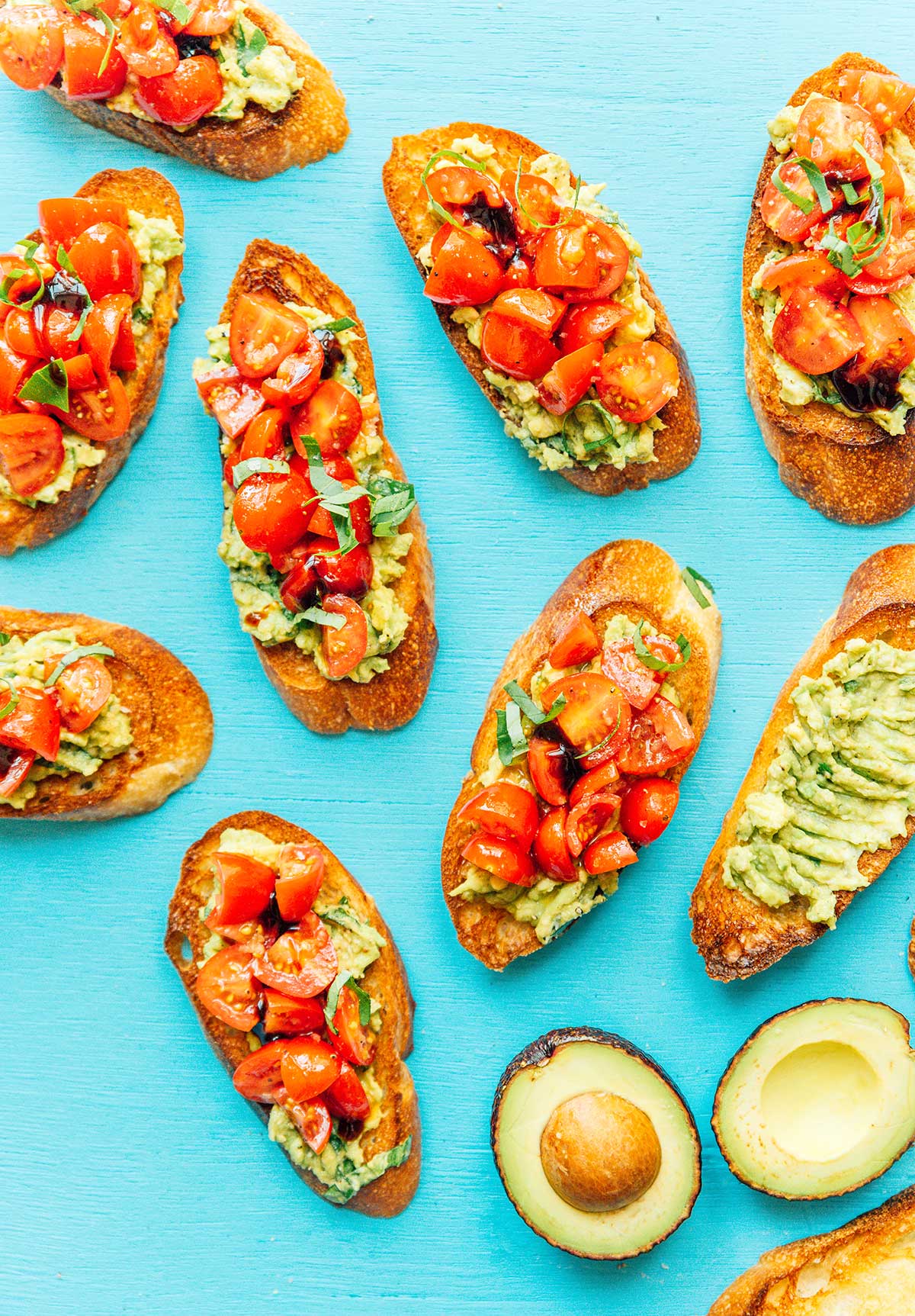 Pieces of assembled avocado and tomato bruschetta scattered around on a blue background