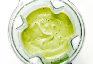 A blender filled with a smooth, green mixture that could easily be mistaken for creamy avocado soup, viewed from above, showcases visible air bubbles and an enticing texture.