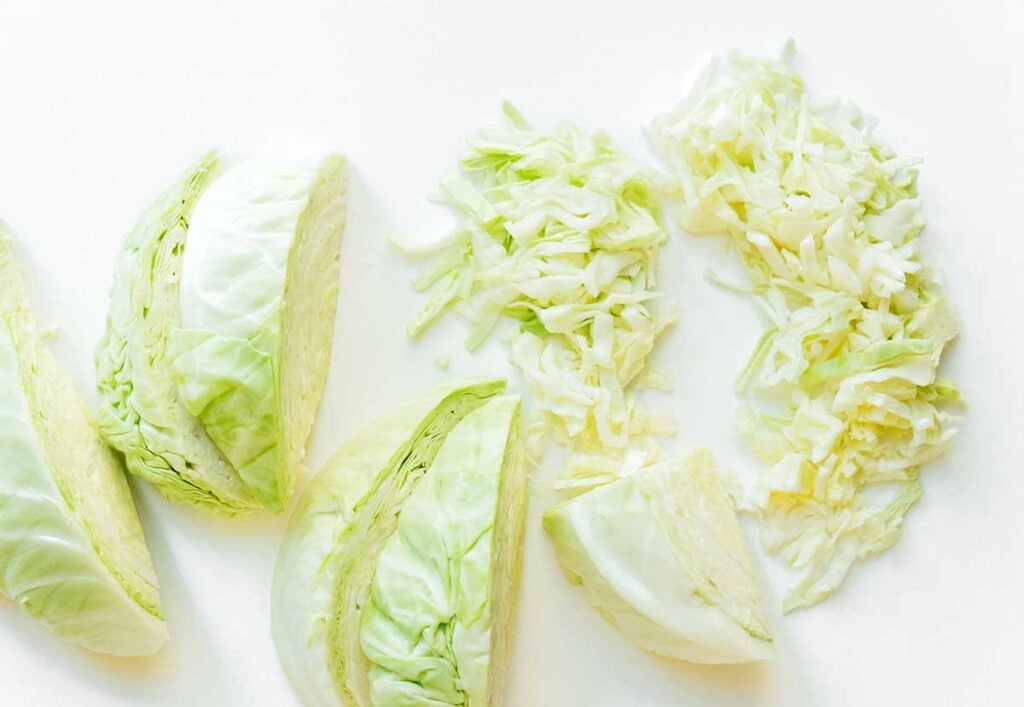 A head of cabbage sliced into 7 quarters, with one quarter completely sliced and another half sliced
