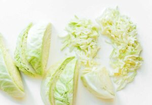 Chopped and sliced cabbage on a white surface, showcasing the textures and cuts essential for learning how to make sauerkraut.