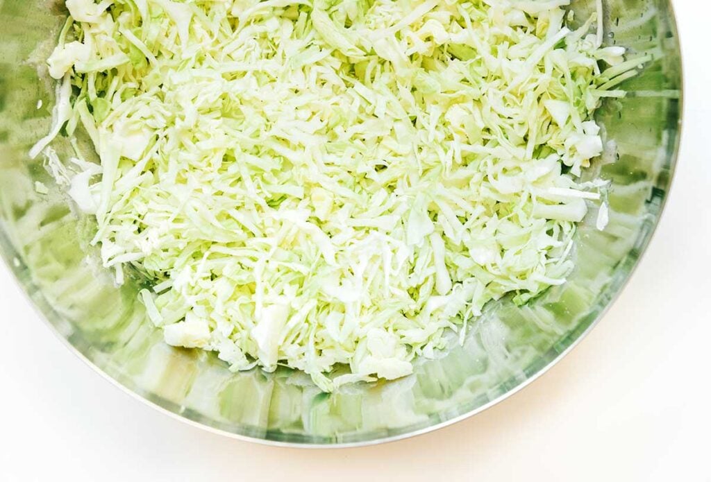 A metal mixing bowl filled with shredded cabbage