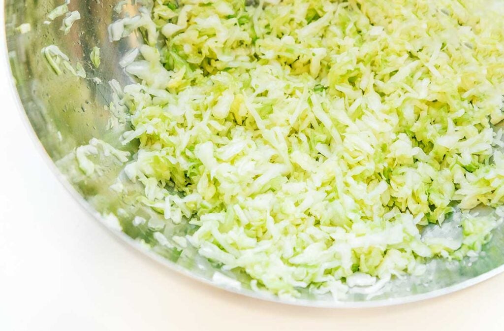 A metal mixing bowl filled with shredded and salted cabbage