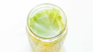 Aerial view of a jar filled with fermenting cabbage, showcasing the brine and cabbage leaves on the surface—an inviting glimpse into how to make sauerkraut at home.