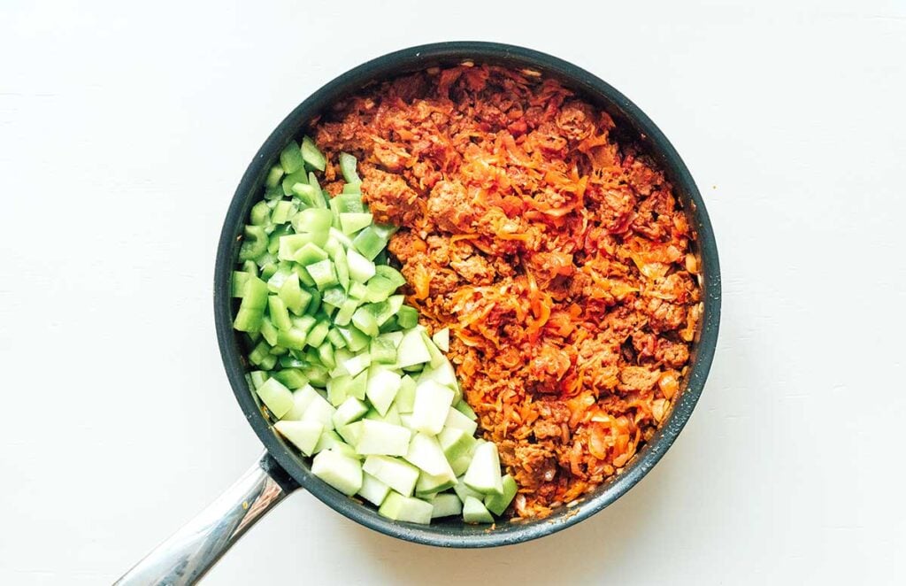 A skillet filled with unstuffed cabbage, diced green apple, and diced green bell pepper