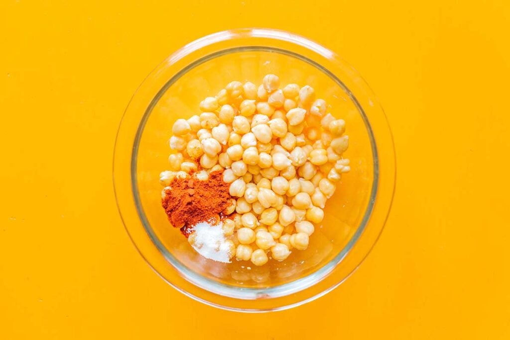 A clear glass bowl filled with chickpeas, paprika, and salt