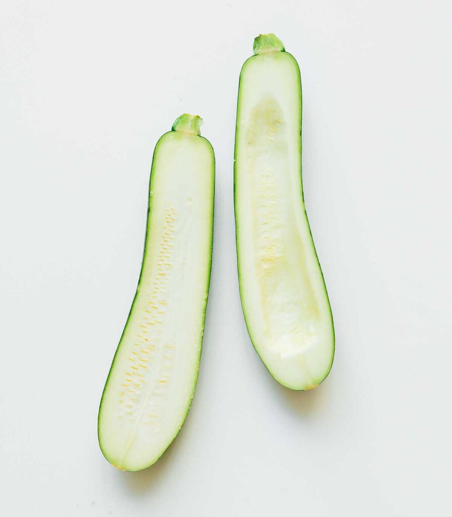 Two zucchini halves on a white background, one with the seedy center removed