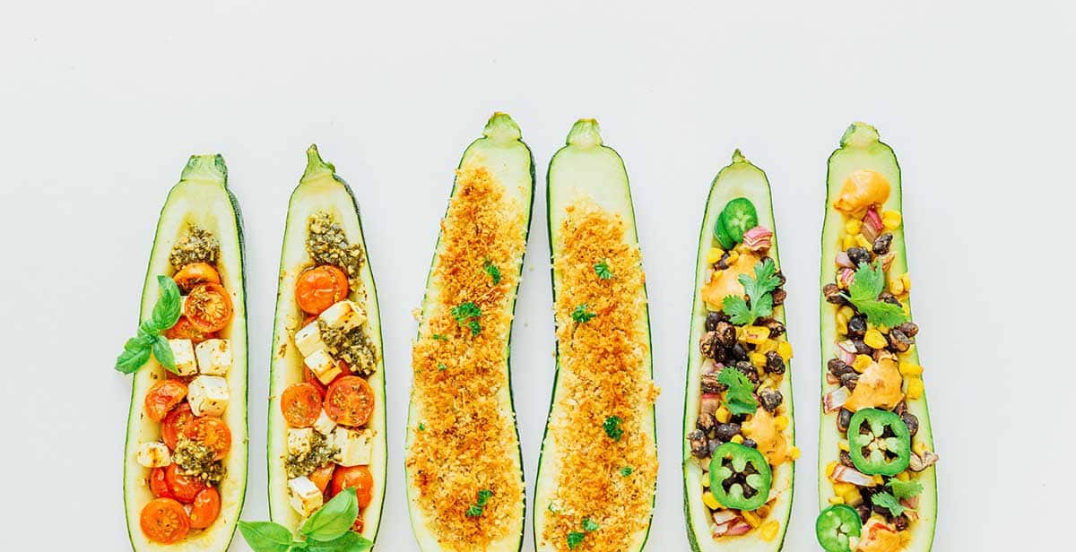 Six stuffed zucchini halves lined up and arranged on a white background
