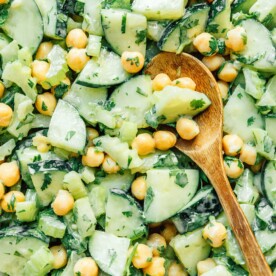 Chickpea veggie salad with cucumbers, celery, and cilantro, mixed in a creamy dressing. A wooden spoon is placed on top.