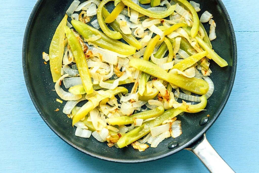 A saute pan filled with cooked green pepper and onion slices