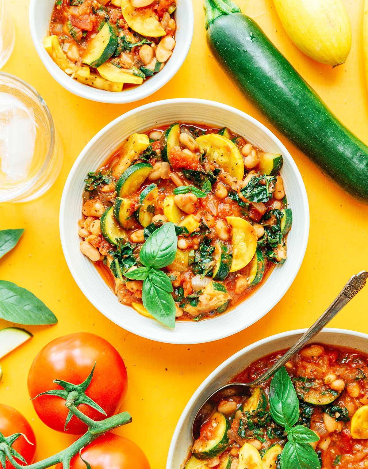 A while bowl filled with zucchini goulash and surrounded by ingredients like tomatoes, zucchini, and squash