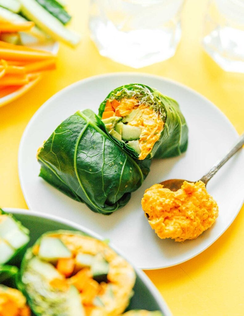 Two buffalo collard leaf wrap halves on a white plate along with a spoonful of buffalo chickpea mix