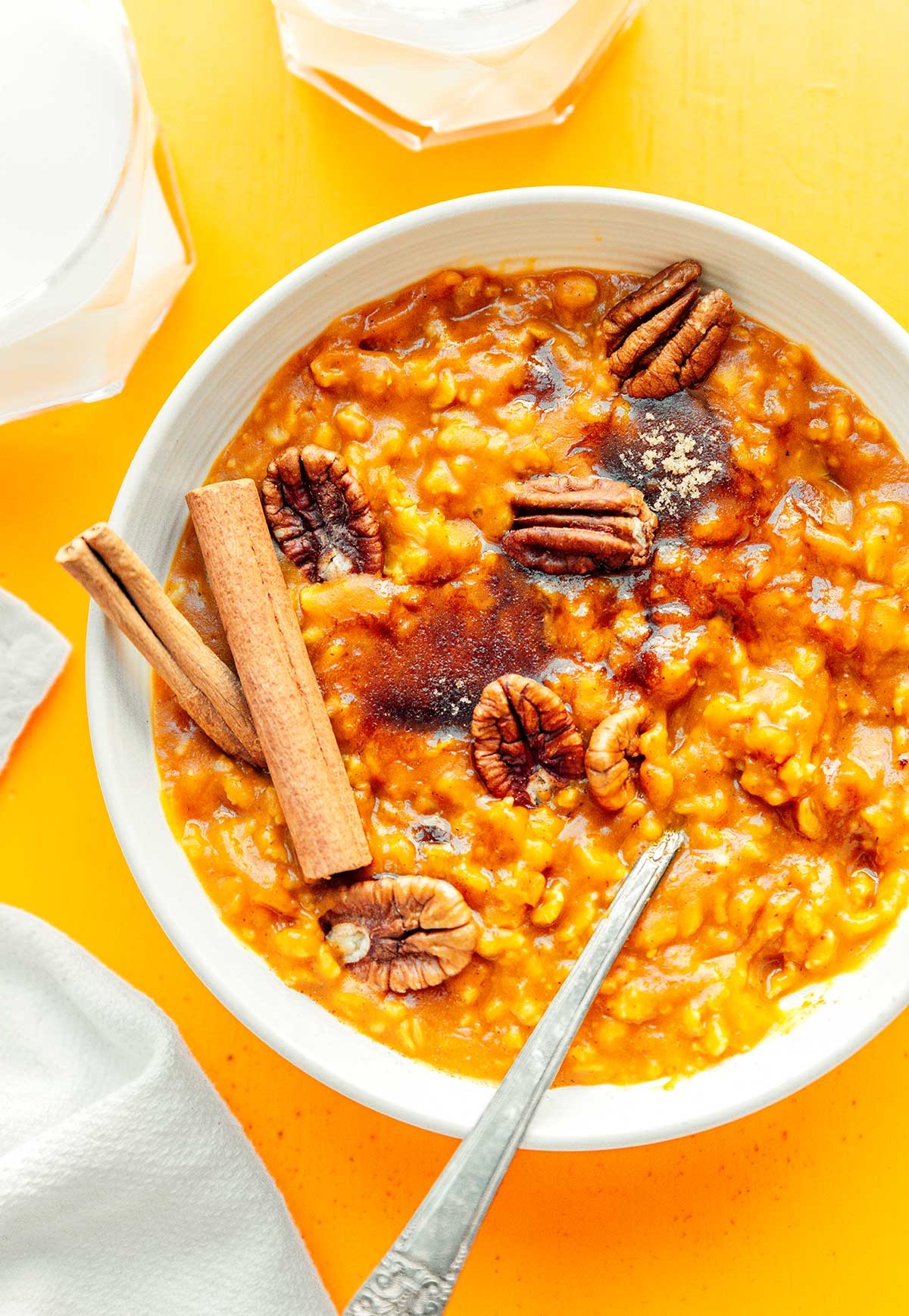 A white bowl filled with pumpkin oatmeal topped with pecans, brown sugar, and cinnamon sticks
