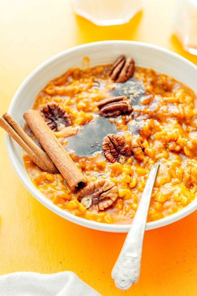 A white bowl filled with pumpkin oats topped with pecans, brown sugar, and cinnamon sticks