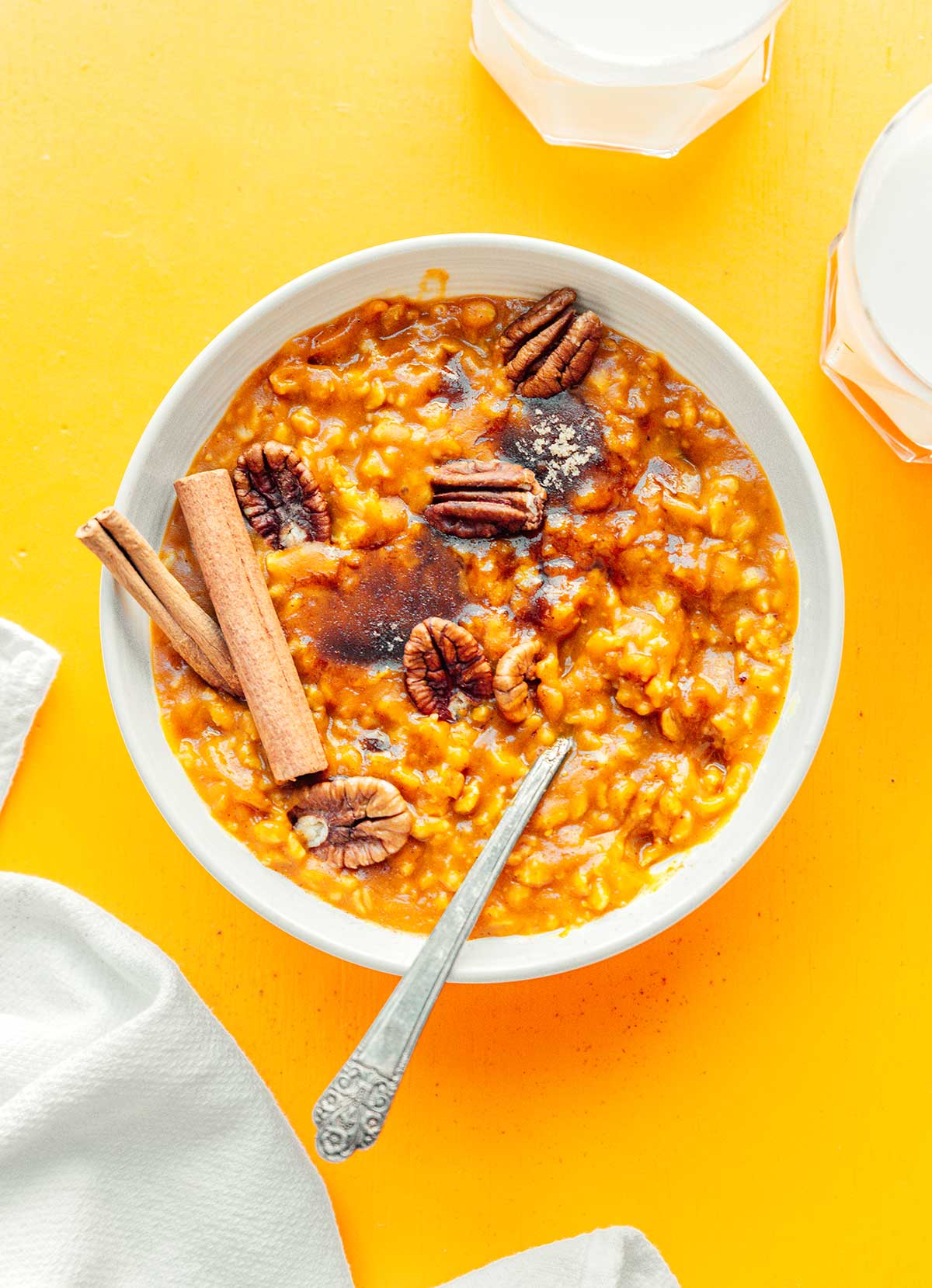 A white bowl filled with pumpkin oatmeal topped with pecans, brown sugar, and cinnamon sticks