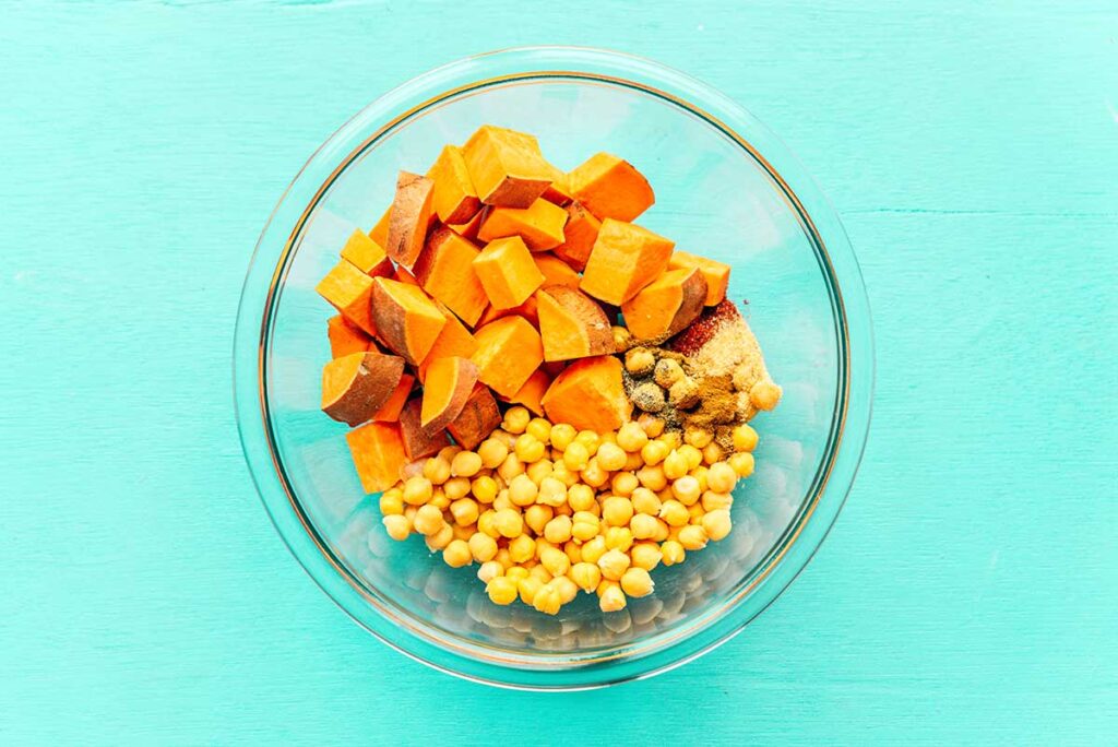 A clear glass bowl filled with chopped sweet potato, chickpeas, and spices