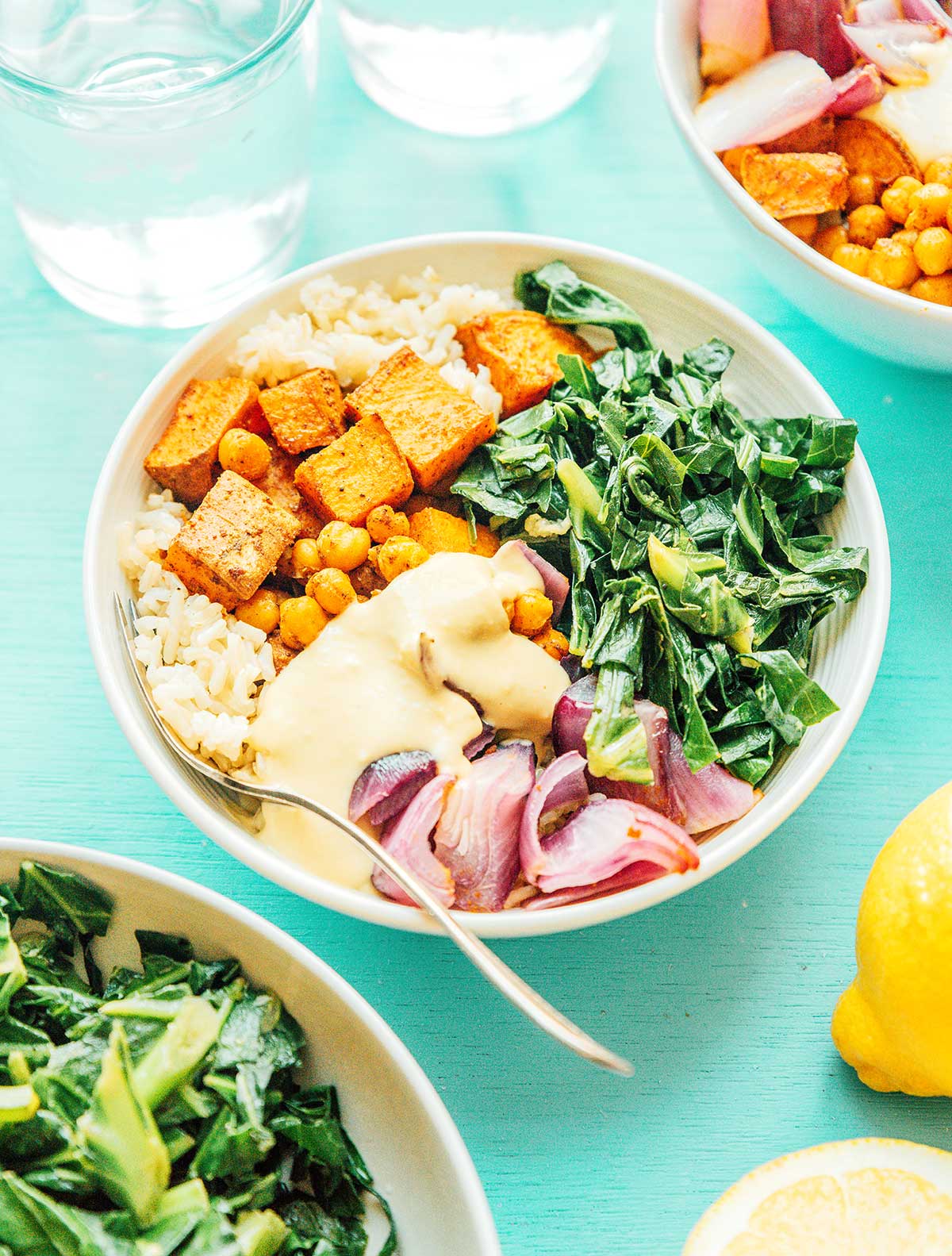 A southern style grain bowl filled with sweet potatoes, veggies, collard greens, red onion, and rice, and topped with a hummus and lemon juice sauce