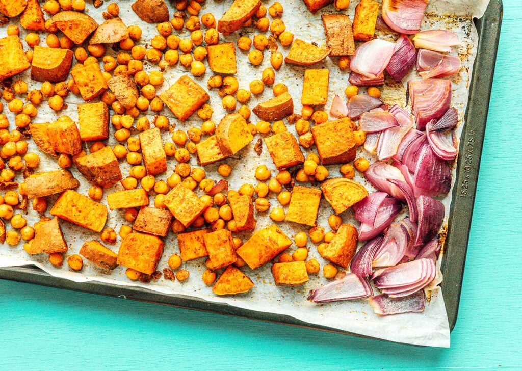 A baking tray filled with cooked chopped sweet potato, red onion, and chickpeas
