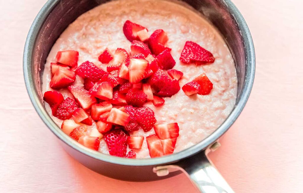 A sauce pot filled with strawberry oatmeal ingredients