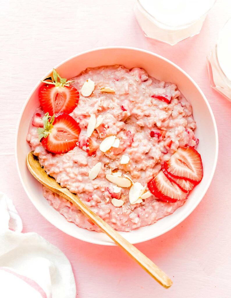 A bowl of strawberry oatmeal topped with strawberry slices and halves and almond slivers
