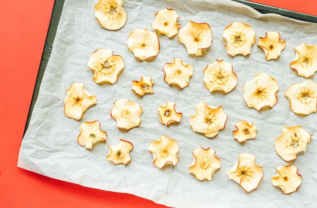 A baking tray lined with parchment paper and filled with an assortment of neatly arranged, fresh out of the oven baked apple chips