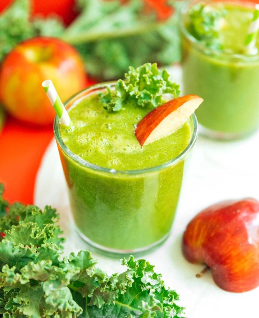 A short glass filled with apple kale smoothie and topped with a piece of kale and an apple slice
