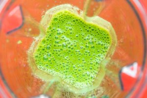 Top view of a blender with bright green, frothy apple kale smoothie partially blended inside a transparent container.