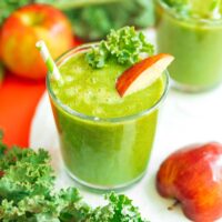 A refreshing apple kale smoothie in a glass with a straw, adorned with a crisp kale leaf and a juicy apple slice. Nearby, vibrant kale leaves and fresh apples complete the wholesome scene.
