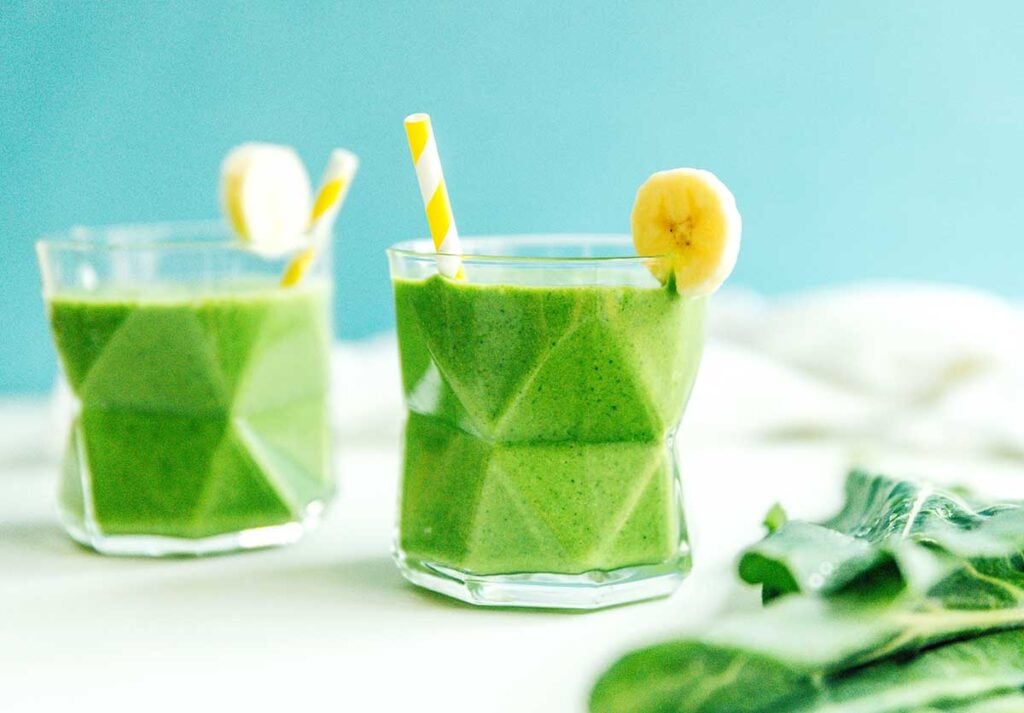 A glass filled with collard green smoothie and garnished with a banana slice