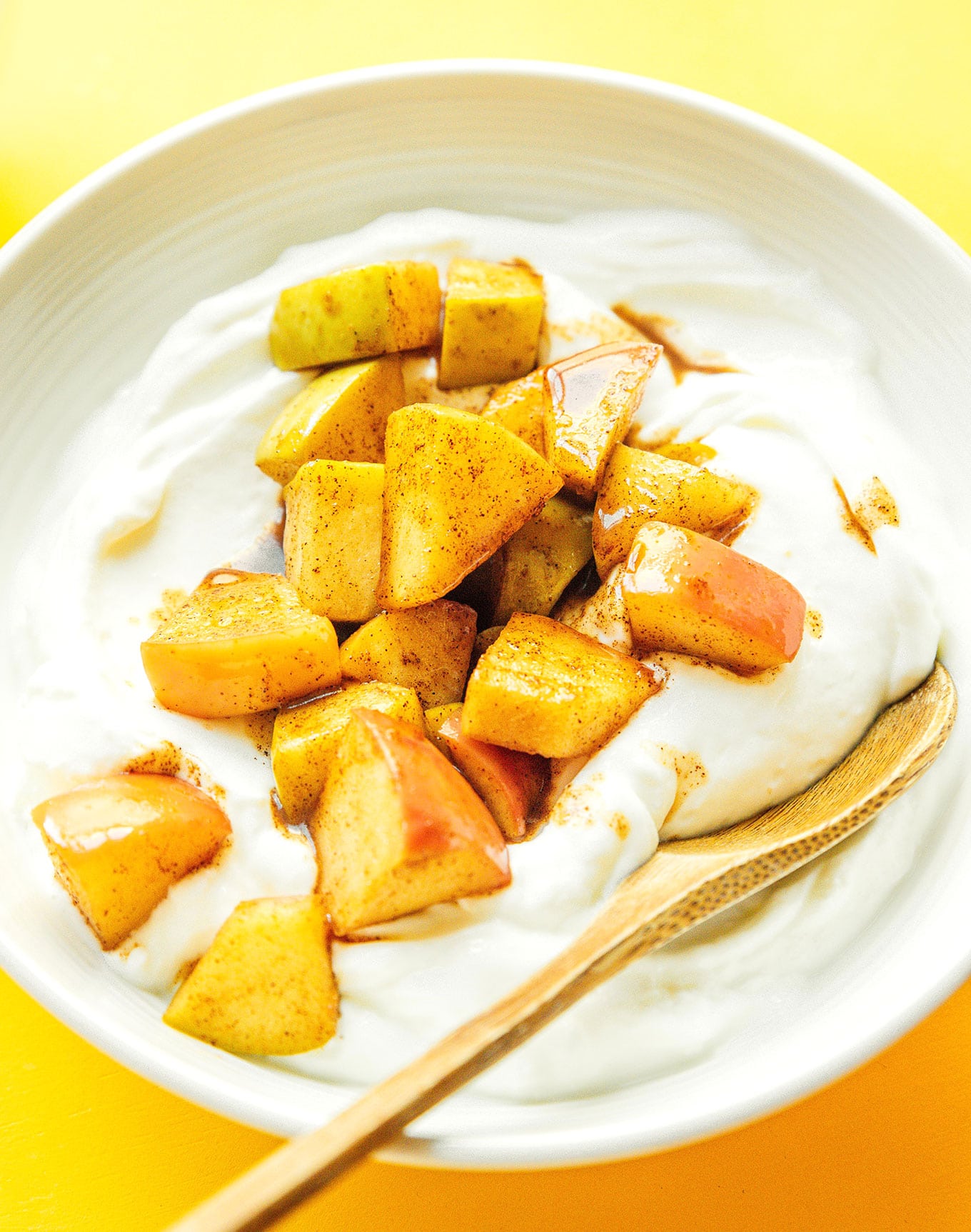 A close up view of a bowl of yogurt topped with stewed apples detailing the texture and spices of the apples