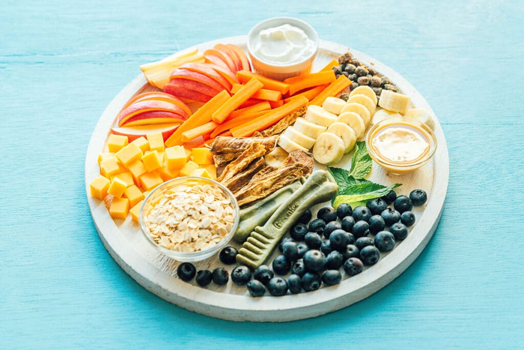 A barkuterie board filled with fruit, veggies, dairy, peanut butter, and dog treats