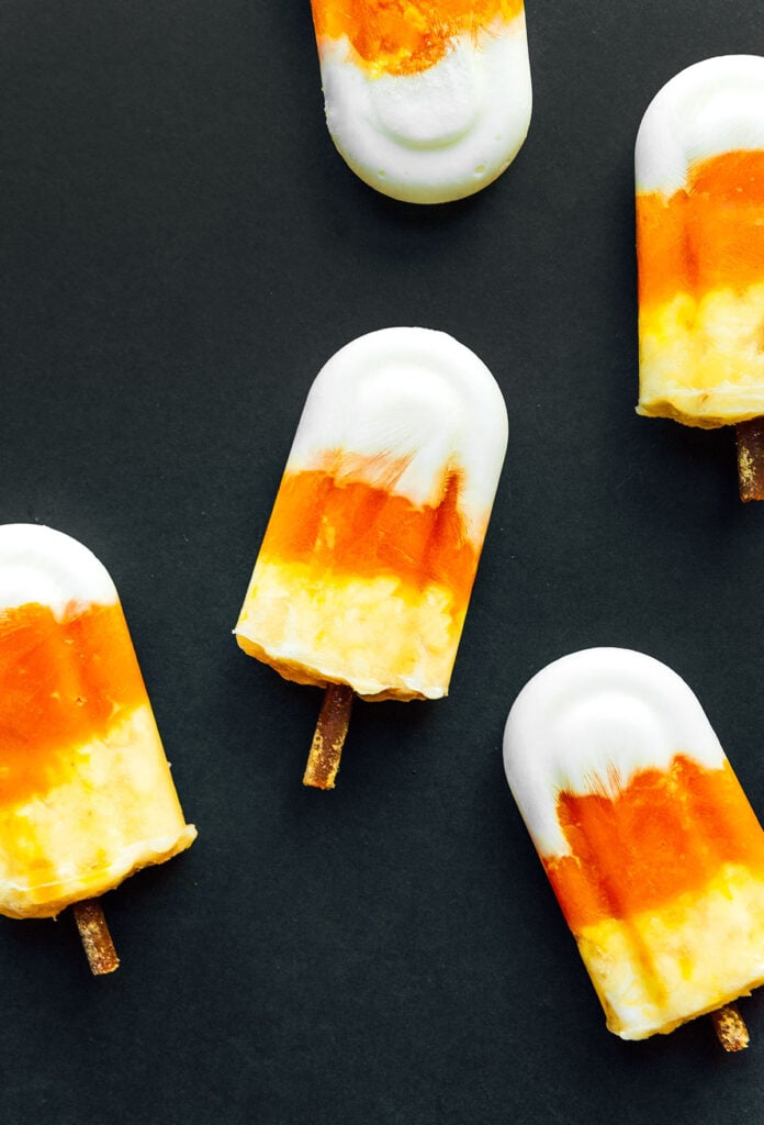 Five candy corn pupsicles arranged on a black background