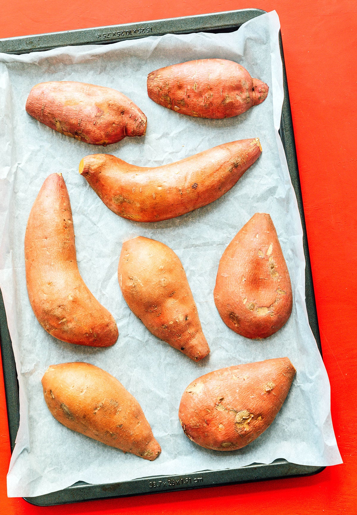 A baking tray lined with parchment paper and topped with halved sweet potatoes lying cut side down