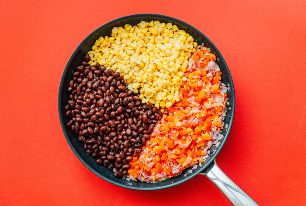 A pan filled with sautéed red onion and red bell pepper along with black beans and corn