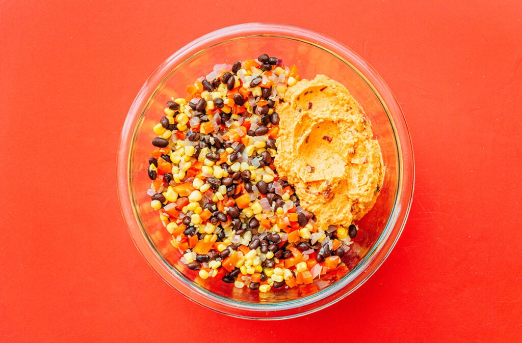 A clear glass bowl filled with the bean and corn mix and the sweet potato flesh mix