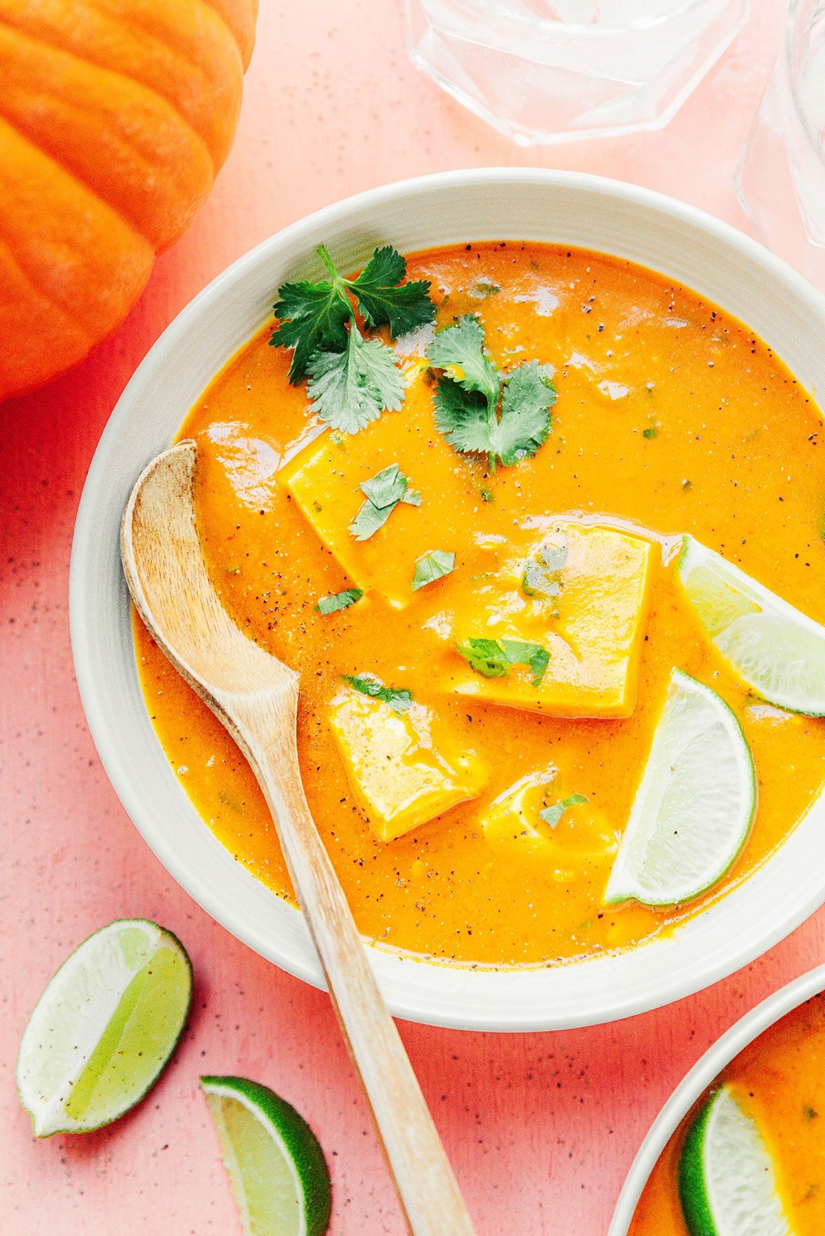A white bowl filled with pumpkin curry garnished with cilantro and lime slices