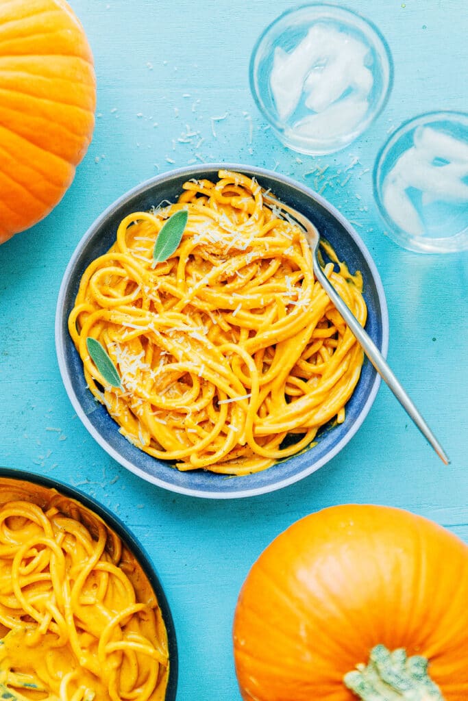 A blue bowl filled with pumpkin pasta topped with parmesan cheese