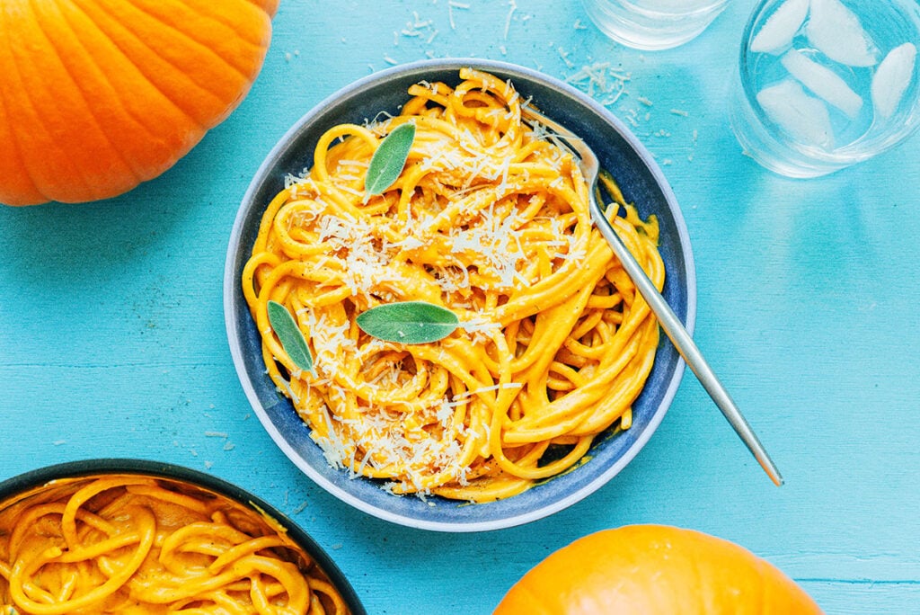 A blue bowl filled with pumpkin pasta topped with parmesan cheese