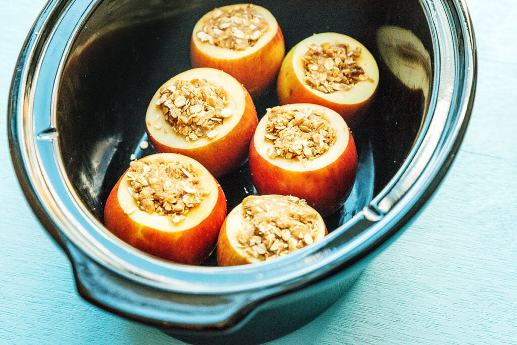 A slow cooker filled with 6 uncooked stuffed apples