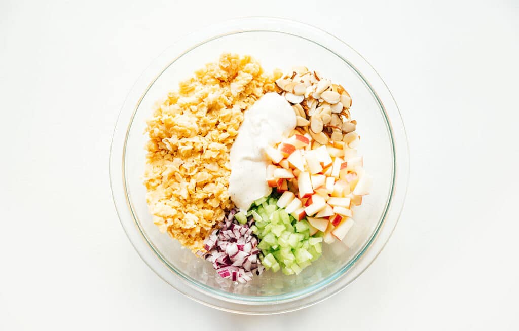 A clear glass bowl filled with unmixed veggie chicken salad ingredients