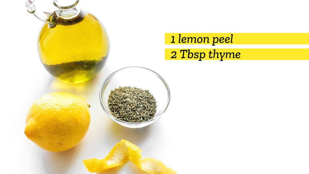 A jar of olive oil, a lemon, a lemon peel, and a small glass bowl filled with thyme