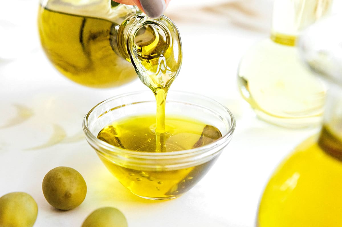 Pouring olive oil from a glass container into a small clear bowl