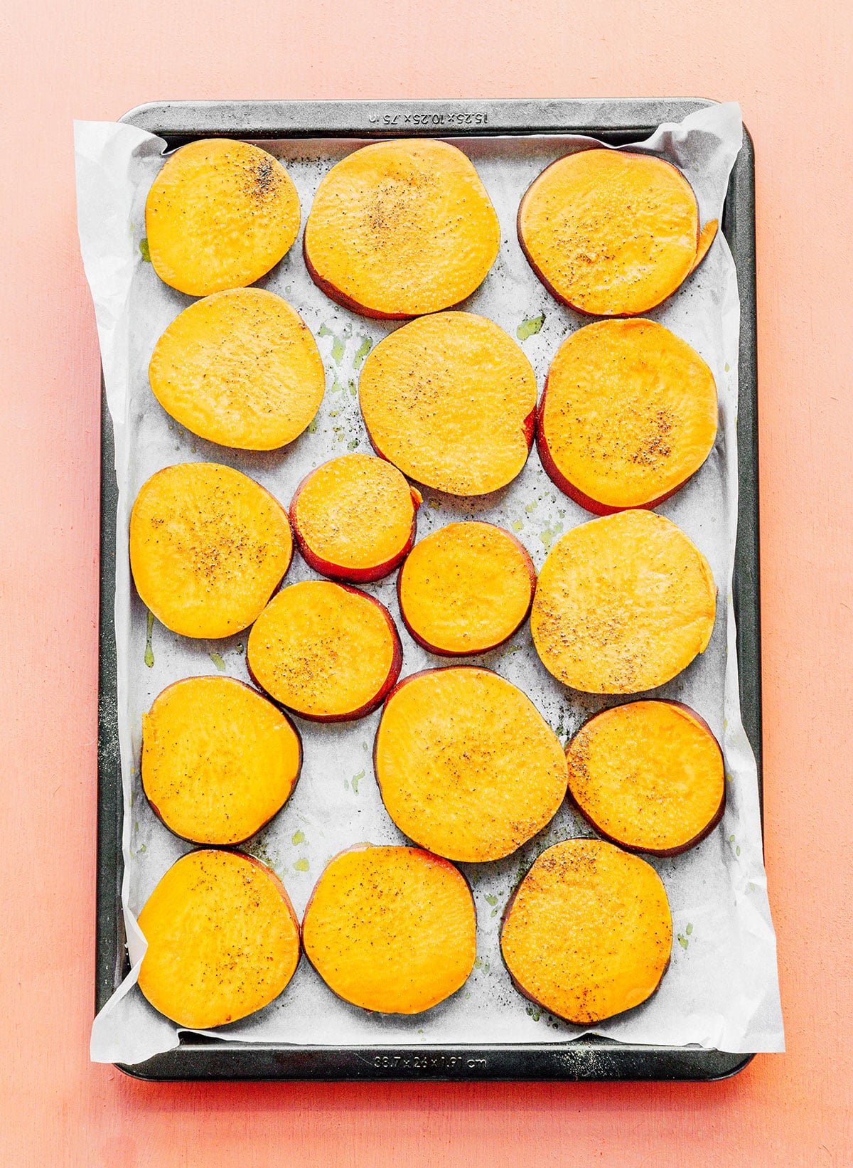 A baking sheet lined with parchment paper and a single layer of sweet potato slices