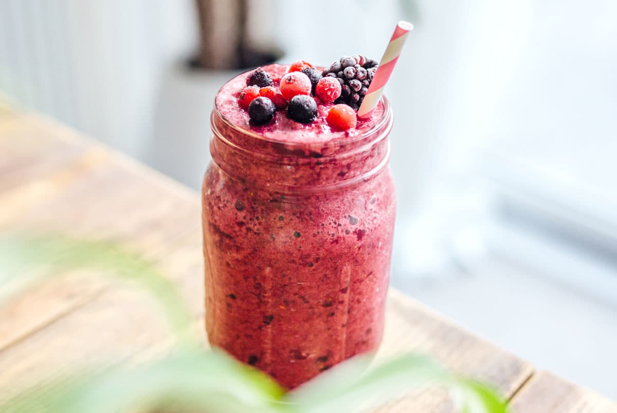 A bright pink berry cabbage smoothie in a mason jar container topped with mixed berries