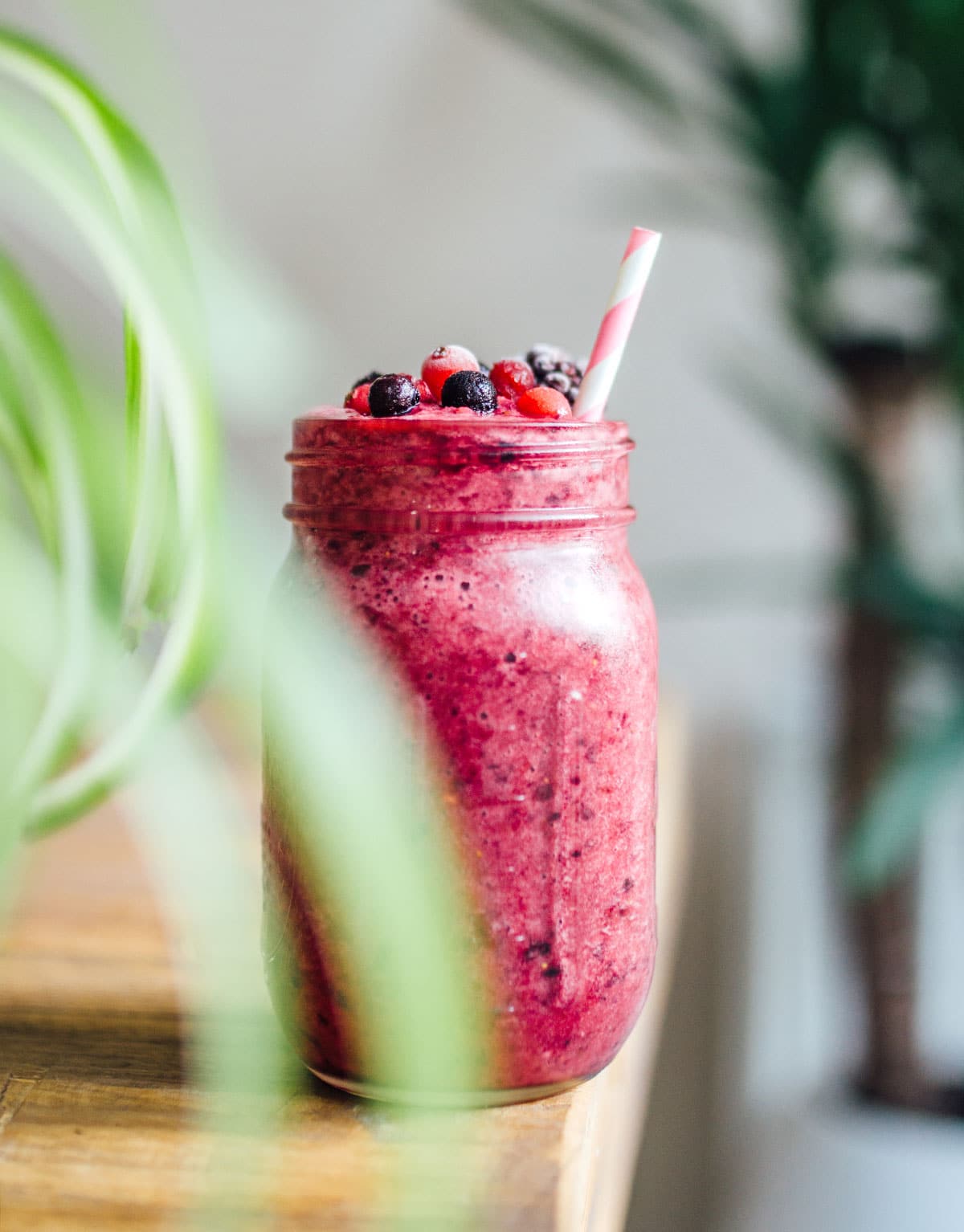 A mason jar filled with a bright magenta berry cabbage smoothie and topped with mixed berries