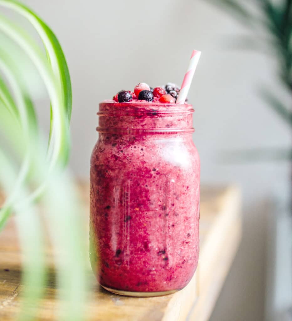 A mixed berry smoothie recipe topped with mixed berries in a mason jar container 
