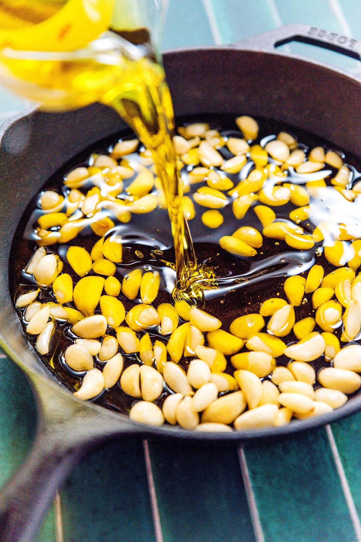Pouring olive oil into a cast iron skillet filled with garlic cloves