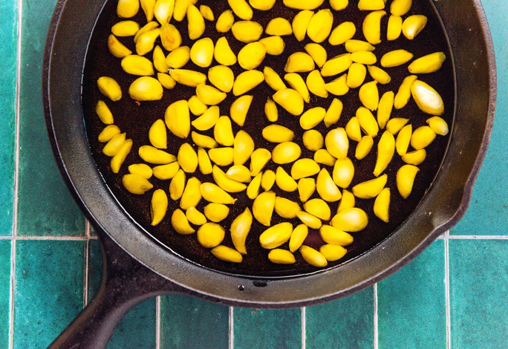 A cast iron skillet filled with olive oil and garlic cloves